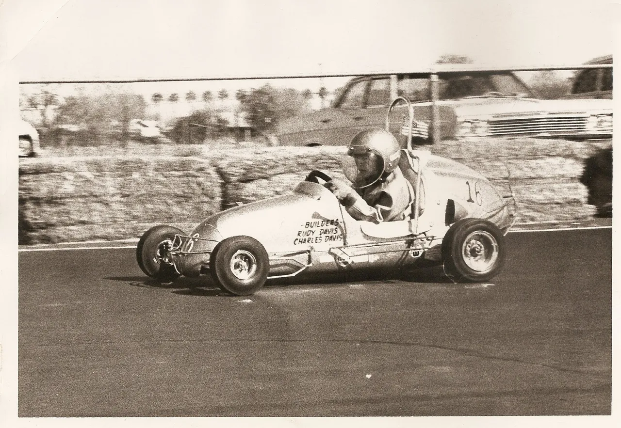 A person in an old race car driving down the road.