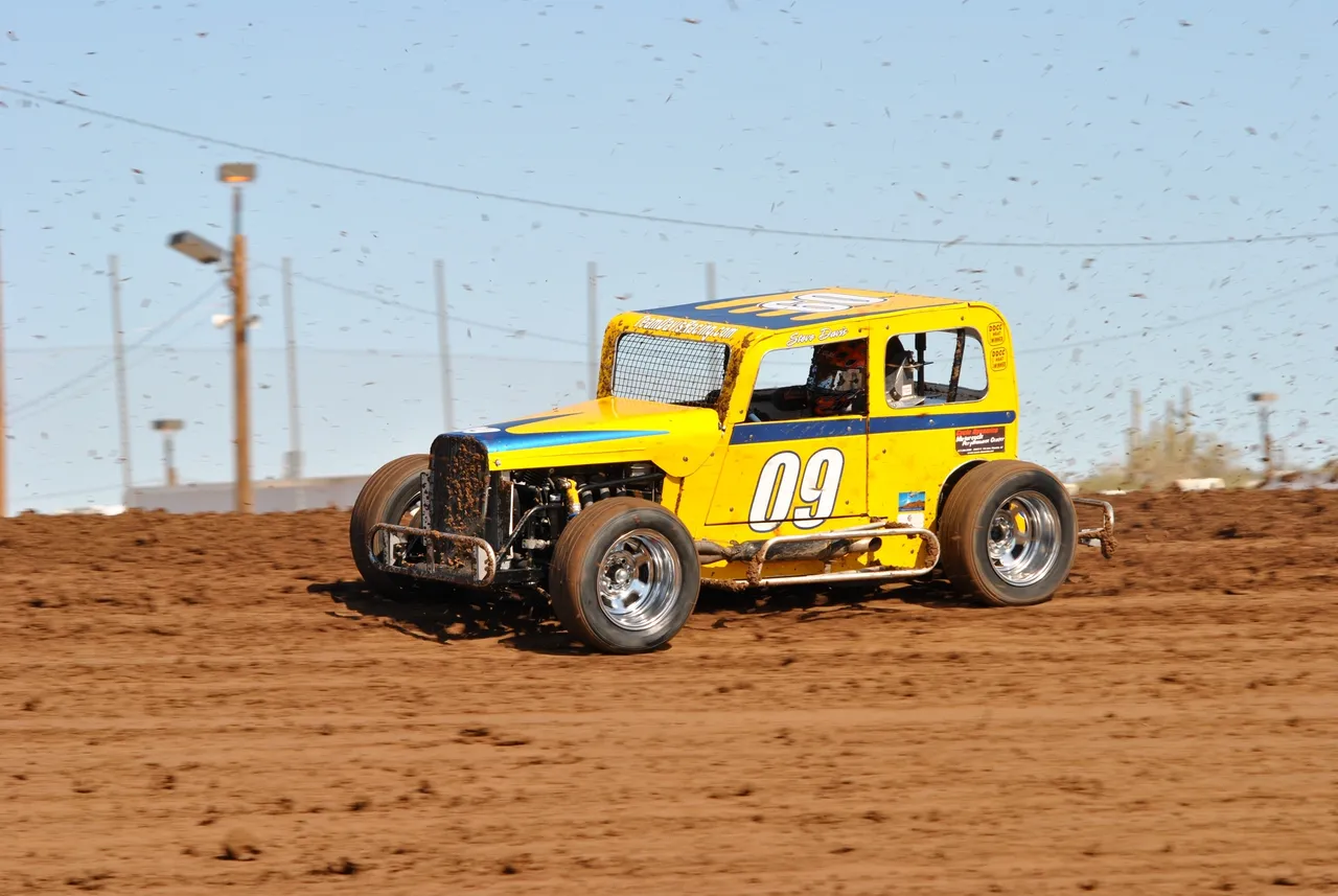 A yellow race car driving down the dirt road.