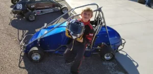 A young boy standing next to an electric go kart.