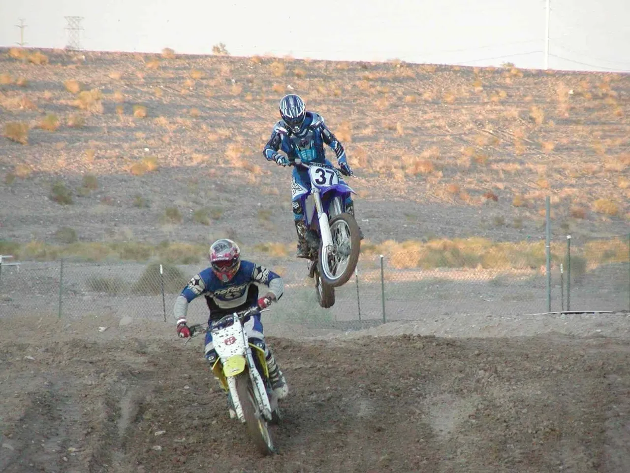 Two people on motorcycles are jumping over a hill.